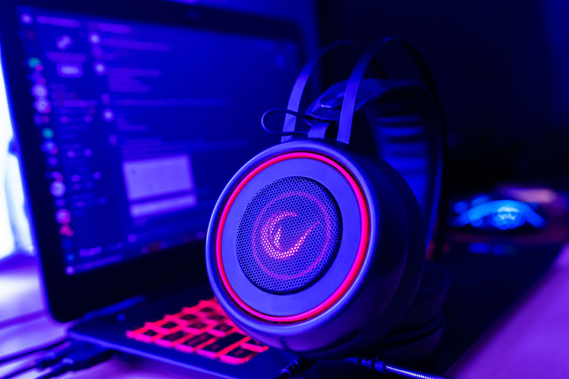 Close-up of gaming headset with neon lighting, placed next to a laptop. Perfect for tech and gaming themes.