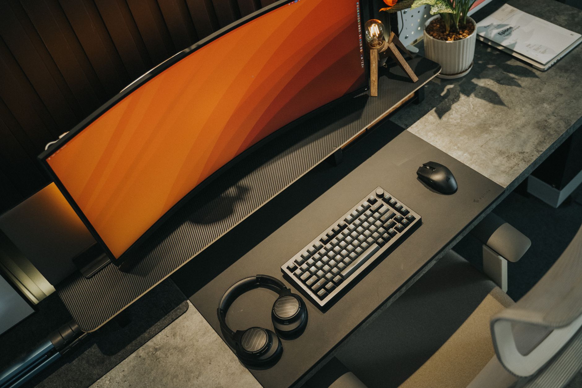 A sleek gaming desk arrangement featuring a curved monitor, keyboard, mouse, and headphones in neutral tones.