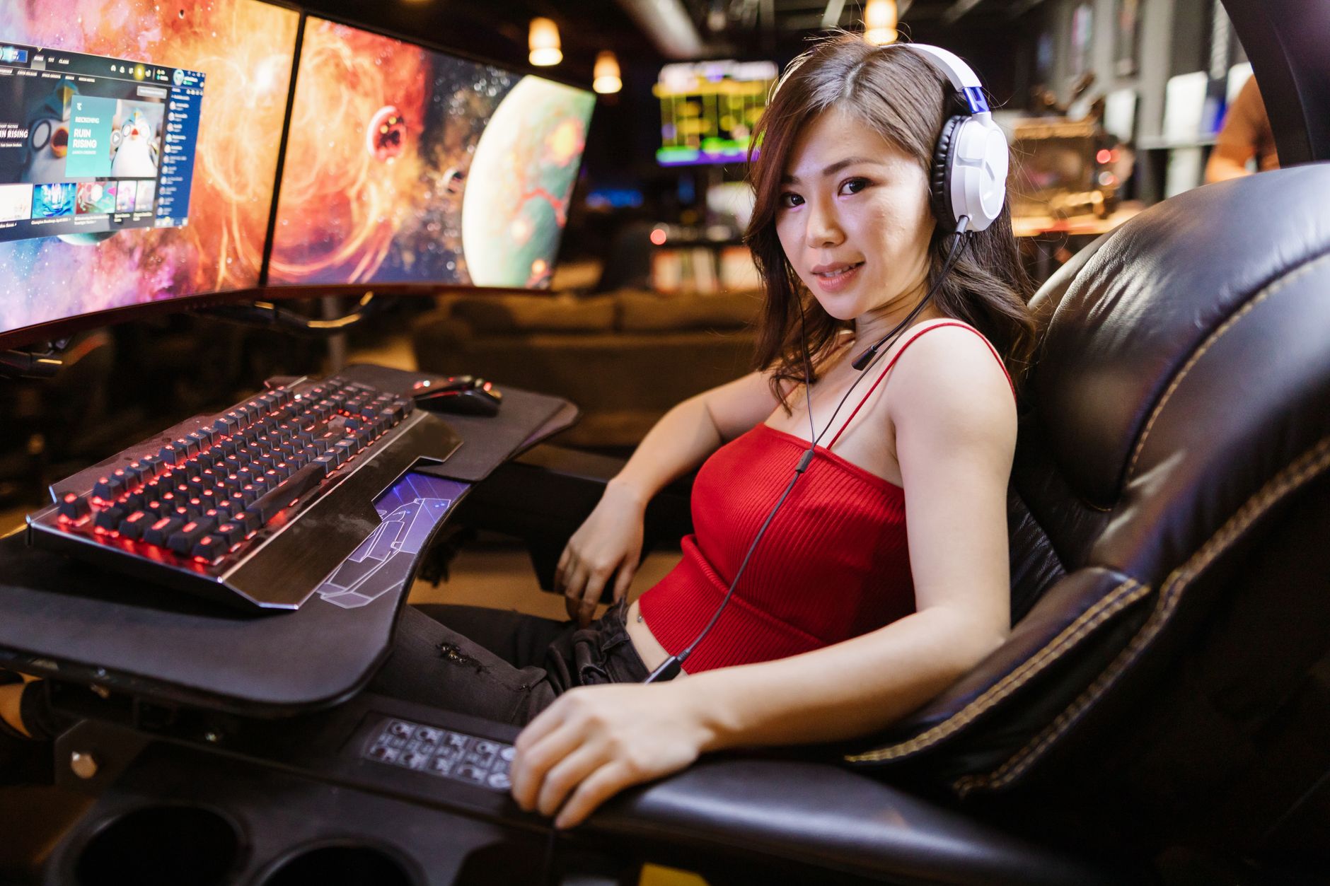 A woman engaged in gaming at a high-tech setup with dual monitors and white headphones.