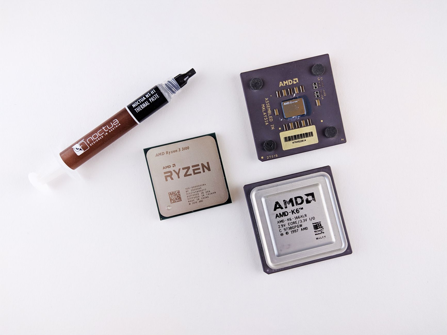 High-angle view of AMD processors and Noctua thermal paste on a white surface.