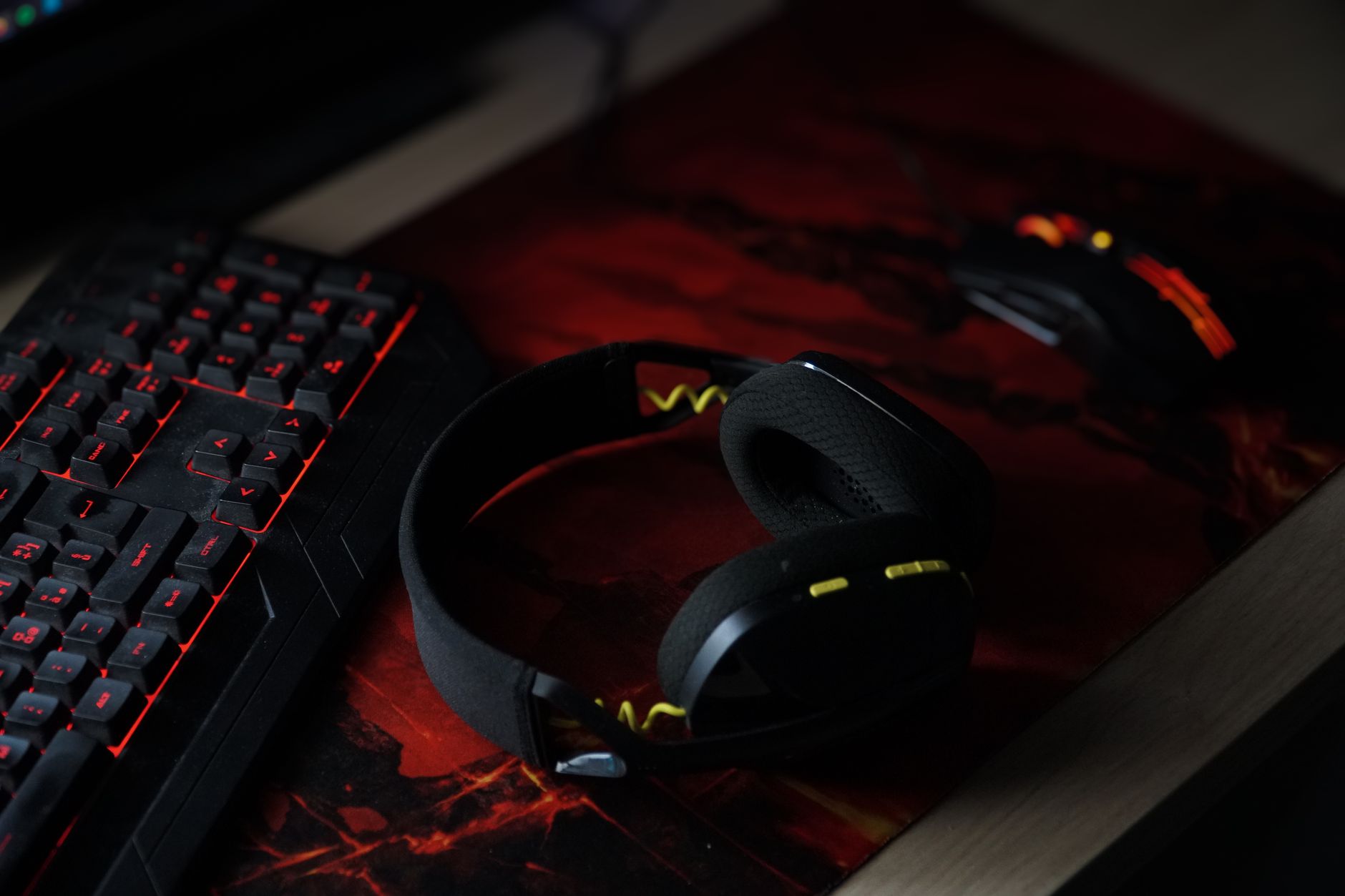 A sleek gaming setup featuring a backlit keyboard, wireless headphones, and a gaming mouse on a vibrant desk pad.