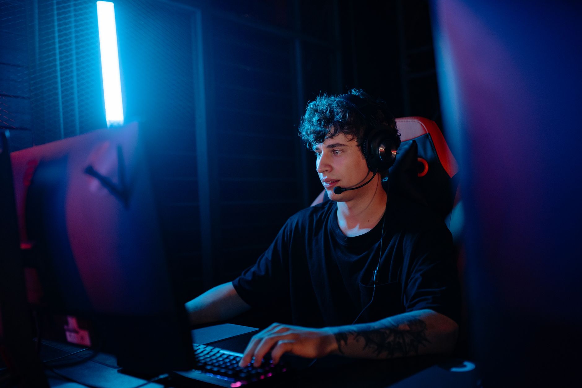A young man intensely gaming with a headset at a computer desk, illuminated by blue light.