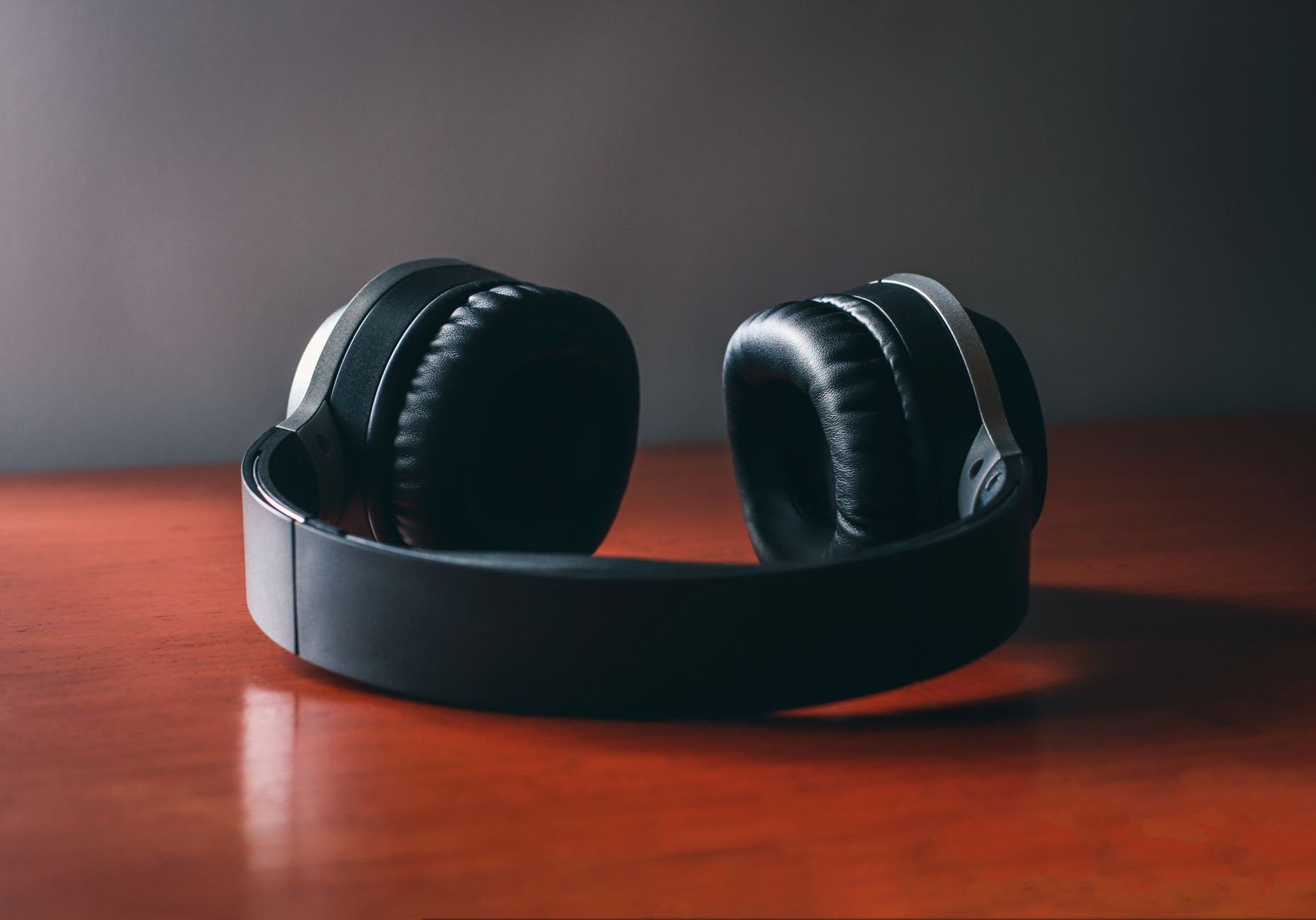Close-up of sleek wireless headphones placed on a polished wooden surface under soft studio lighting.