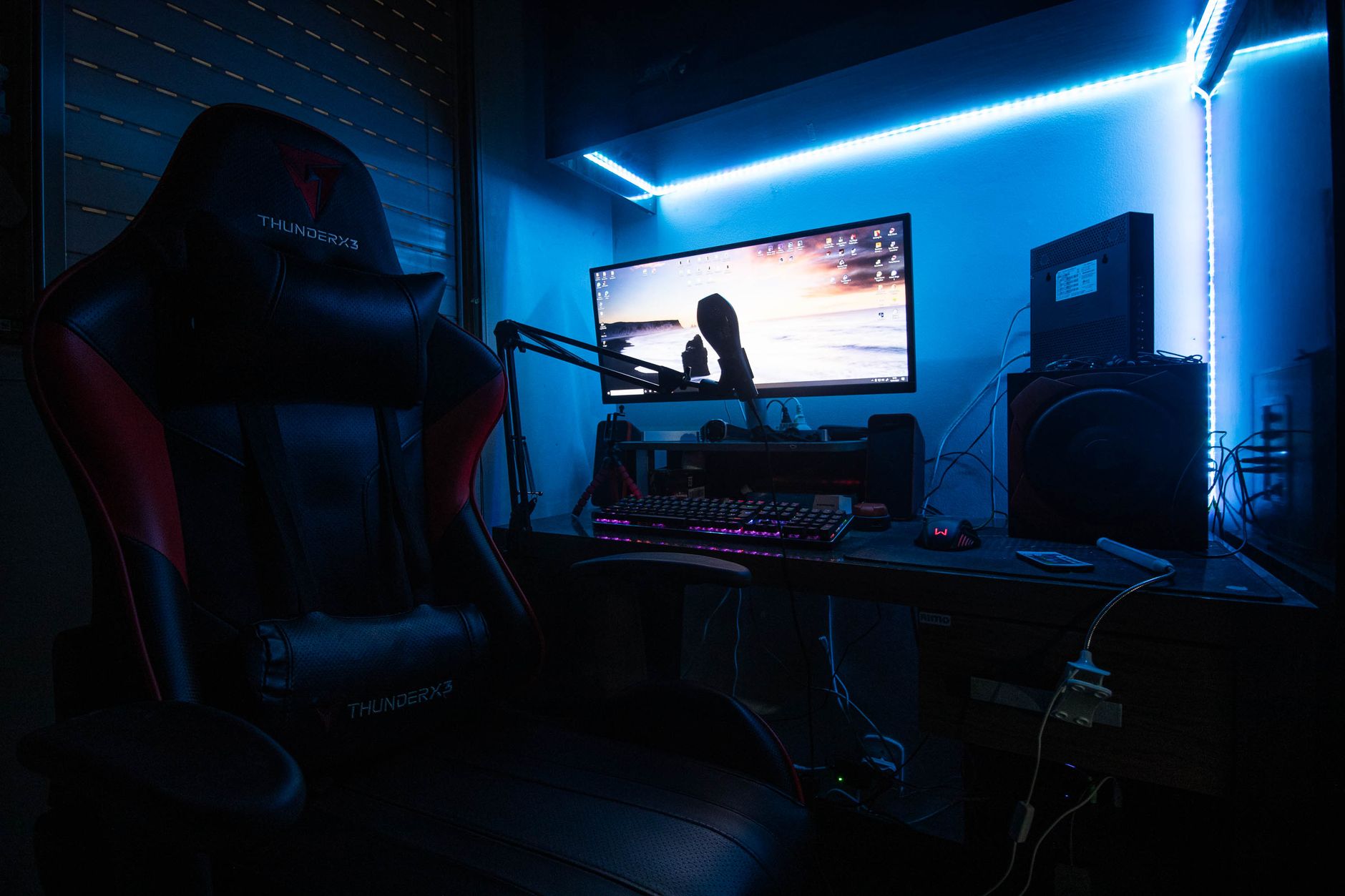 A sleek gaming desk with a monitor, gaming chair, and LED lights creating an immersive environment.