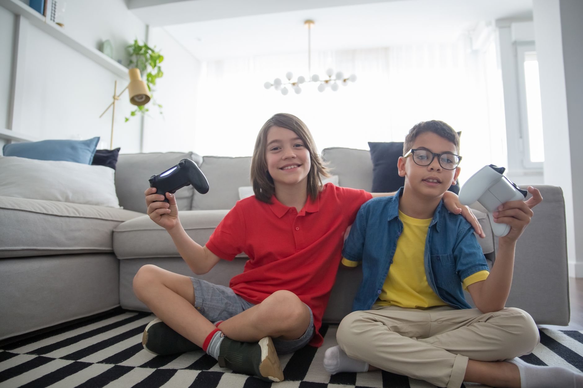 Two children playing video games indoors, sitting on a cozy rug with game controllers in hand.