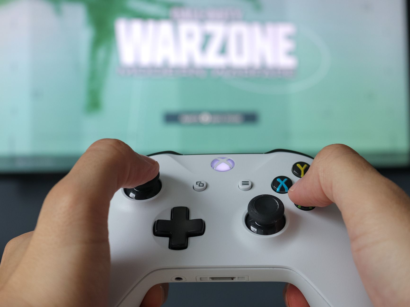 A close-up of hands holding an Xbox controller against a game screen, highlighting the gaming experience.