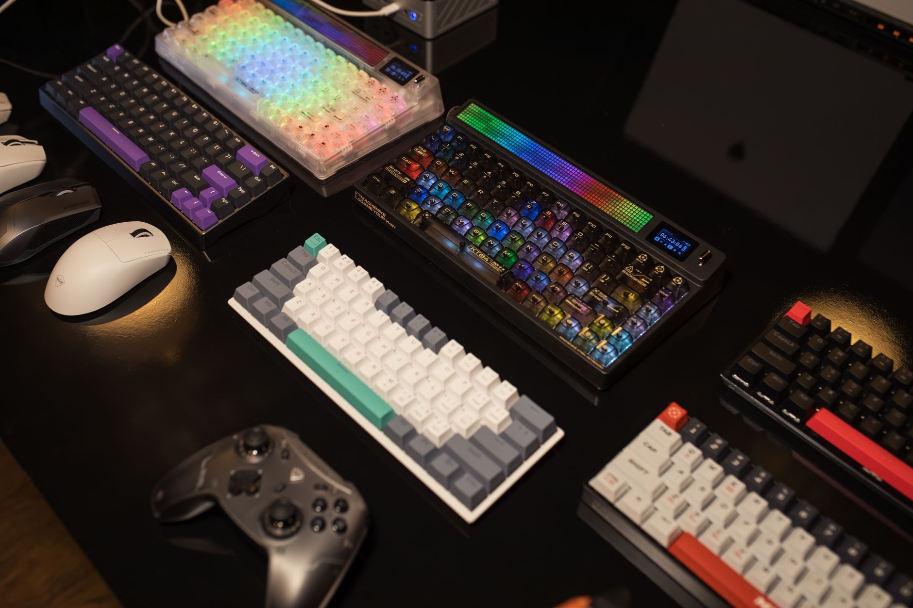 A collection of mechanical keyboards and gaming accessories displayed on a table, illuminated by vibrant RGB lighting.
