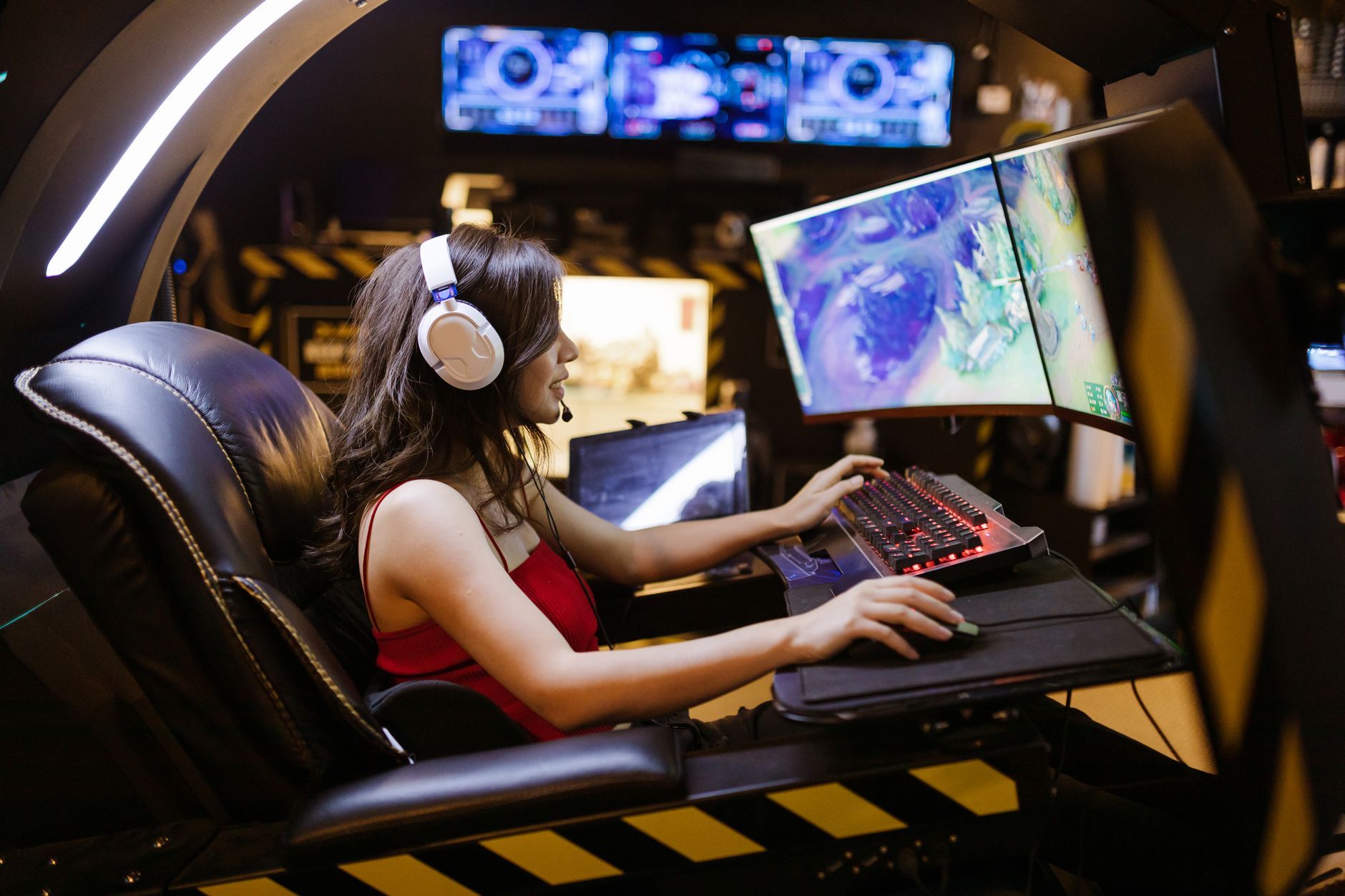 Young woman intensely focused on playing a multiplayer online game at a high-tech gaming station with a curved monitor.