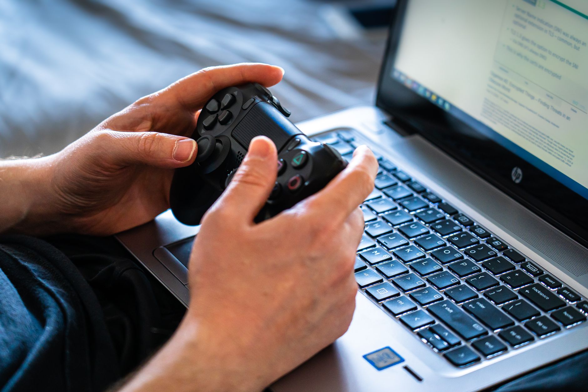Person holds a gaming controller while interacting with a laptop, emphasizing modern gaming technology.